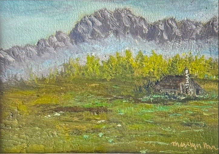 A framed landscape painting displayed on a laptop screen. The painting depicts a green field with yellow wildflowers, a small cabin, and gray mountains under a blue sky.